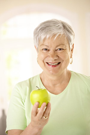 Closeup portrait of healthy senior woman holding apple, looking at camera, smiling.の写真素材