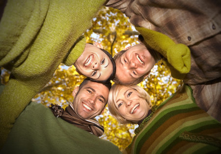 Group of happy friends standing with their heads together in autumn forest, smiling. Low angle...