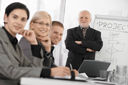 Confident businesspeople smiling at camera at training, senior executive standing at background with arms folded.の写真素材