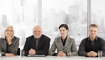 Formal businessteam portrait of different generations sitting at meeting table, smiling at camera. Formal businessteam portrait of different generations sitting at meeting table, smiling at camera.