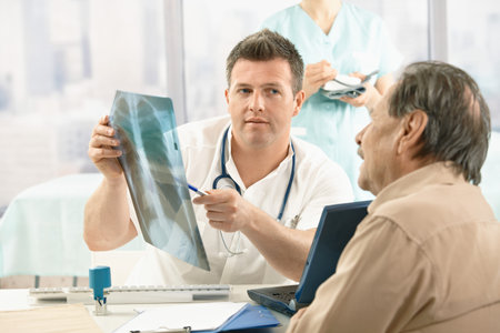Doctor showing diagnosis of x-ray image to older patient sitting at office desk.