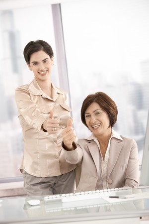 Smiling businesswomen giving thumb up in officeの写真素材