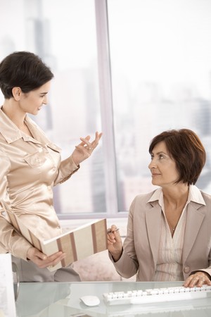 Female assistant showing documents to senior businesswoman in office, smiling.の写真素材