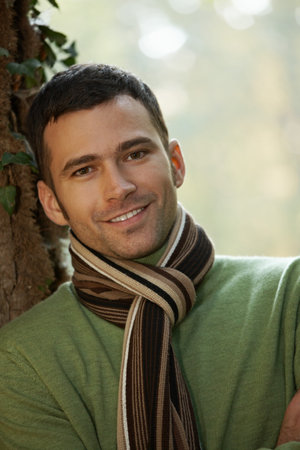 Outdoors portrait of happy young man standing in autumn park at tree.の写真素材
