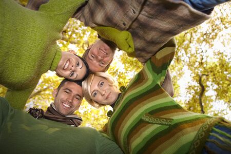 Happy friends standing with their heads together in autumn forest, smiling. Low angle view.の写真素材
