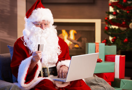 Santa Claus using computer purchasing Christmas presents on internet paying with credit card.の写真素材