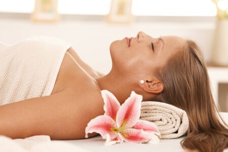 Closeup portrait of beautiful young woman lying on massage bed at spa, smiling.の写真素材