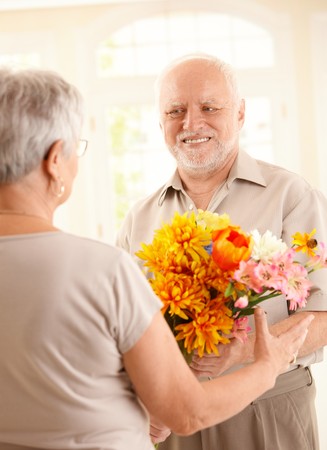 Smiling senior man bringing flowers to older woman.の写真素材