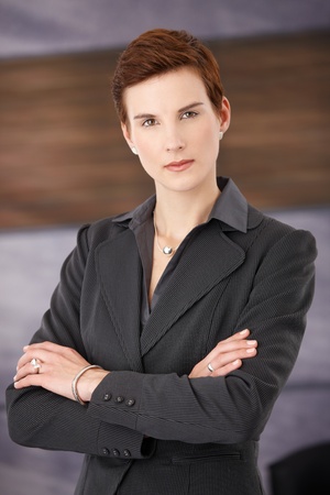 Trendy determined businesswoman standing in office with arms folded, looking at camera.の写真素材