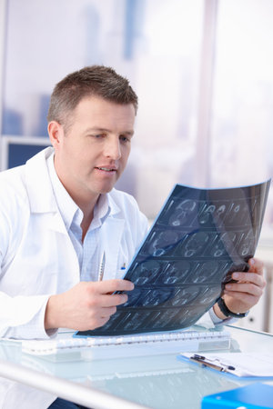Male doctor looking at x-ray image in bright office.