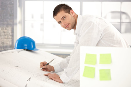 Handsome young engineer drawing plans in bright office.