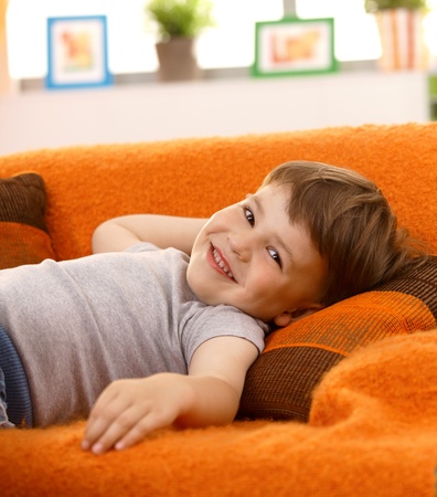 Cute little boy lying on couch at home, laughing, looking at camera.の写真素材