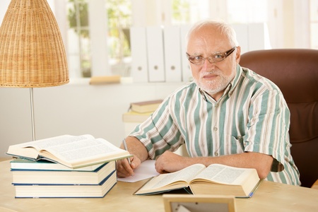 Portrait of older man working at his study, taking notes, using books, looking at camera.の写真素材