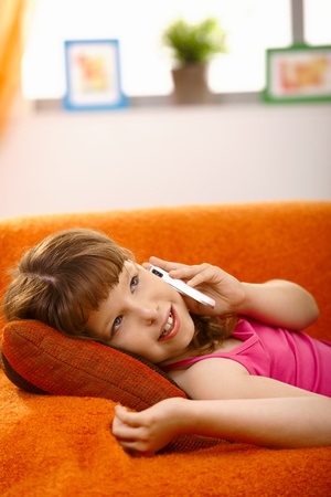 Schoolgirl lying on couch talking on mobile phone, smiling,の写真素材