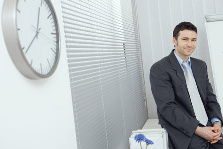Portrait of businessman wearing grey suit and blue shirt, sitting in office, smiling.