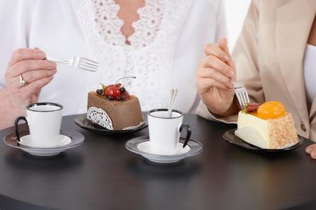 Two women sitting at coffee table, eating cake, drinking coffee, face is not visible.の写真素材
