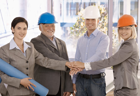 Team portrait of happy architects standing in office, holding hands together expressing teamwork and...