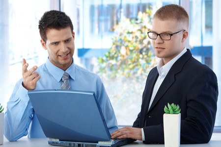 Coworkers discussing work in office, businessmen using laptop computer, concentrating on screen.の写真素材