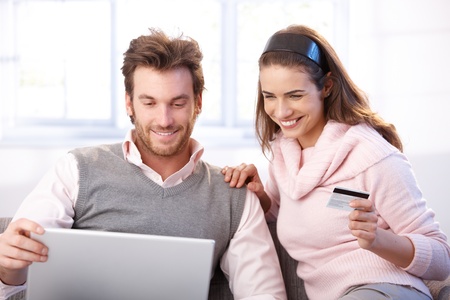Happy young couple shopping online, using laptop and credit card, smiling.の写真素材