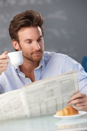 Portrait of goodlooking man drinking coffee and reading morning papers at home.の写真素材
