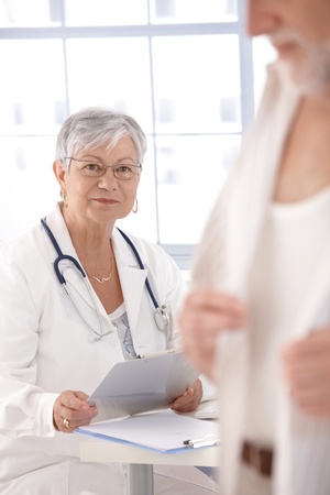 Senior female doctor sitting at desk, looking at patient.の写真素材