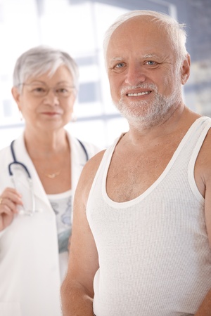 Elderly man ready for examination, female doctor in the background.の写真素材