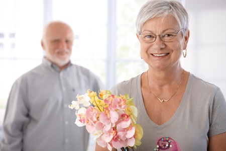 Portrait of smiling senior woman holding flowers, man at background.の写真素材