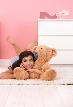 Pretty girl laying on floor, hugging huge soft toy bear, talking on mobile phone.の写真素材
