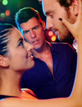 Desperate jealous man looking at flirting couple in discotheque.の写真素材