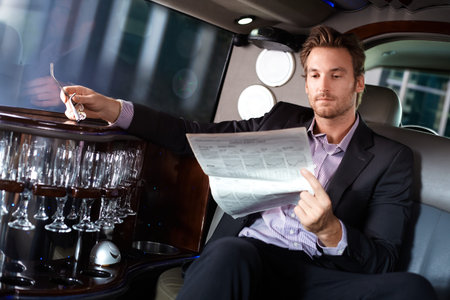 Handsome young man sitting in limousine, reading newspaper. 