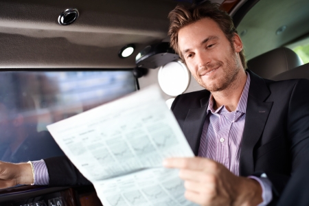 Happy young man reading newspaper in luxury car, smiling.の写真素材