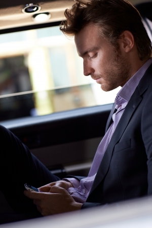 Smart man texting on cellphone, sitting in elegant car.の写真素材