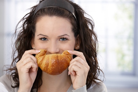 Cheerful woman posing with croissant smile.の写真素材