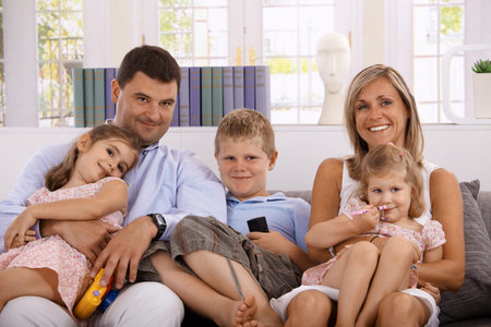 Happy family sitting on sofa at home, smiling, having three children.