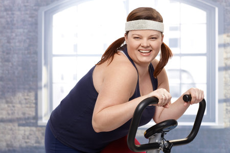 Happy fat woman training on exercise bike, smiling.の写真素材