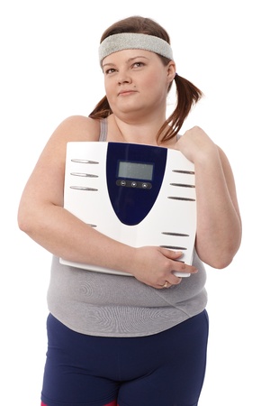 Fat woman in sportswear holding a scale in hands, daydreaming.の写真素材