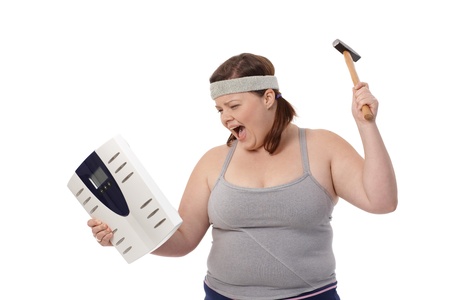 Angry fat woman punching scale by hammer, shouting.の写真素材