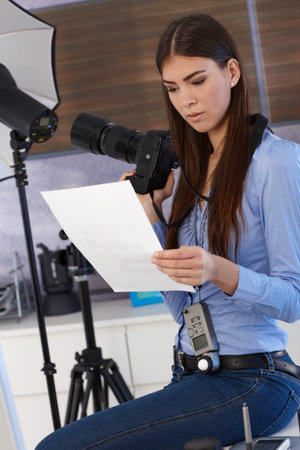 Pretty photographer woman sitting in studio examining photo handheld, holding camera.