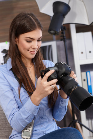 Smiling photographer at work, checking camera setting in studio. 