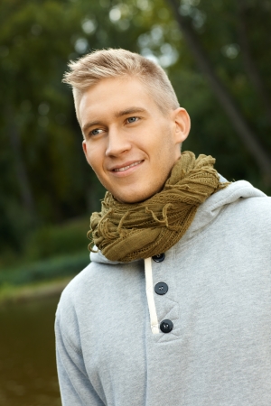 Autumn portrait of young blonde man in park, looking away, smiling.の写真素材