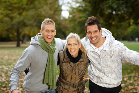 Attractive young friends having fun in autumn park, smiling, looking at camera.