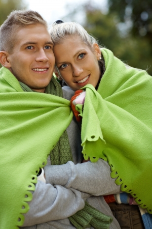 Smiling young couple on cold autumn day, covered by blanket.の写真素材