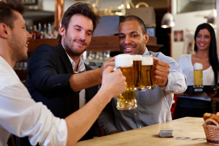 Happy friends clinking with beer mugs in pub, smiling.の写真素材