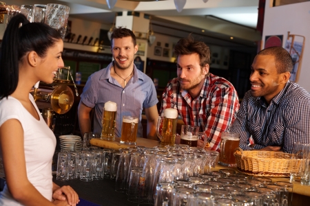Young men sitting at counter in pub, drinking beer and flirting with attractive bartender.の写真素材