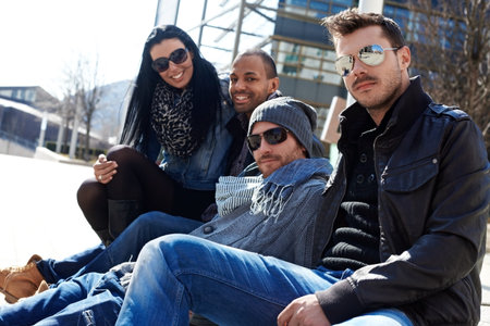 Group of trendy young people sitting outside of building, enjoying springtime sunshine 