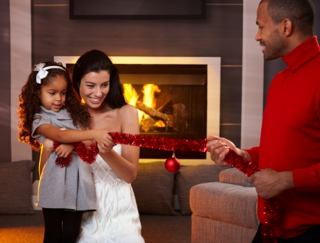 Happy interracial family having fun at home by fireplace, playing with christmas decorations.の写真素材