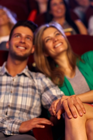Happy young couple sitting at cinema, focus on hands and female leg.の写真素材
