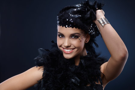 Happy beauty in party outfit, posing with black sequin hat and feather boa, smiling. 