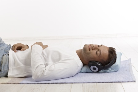 Young man lying on floor eyes closed, listening to music through headphones.の写真素材