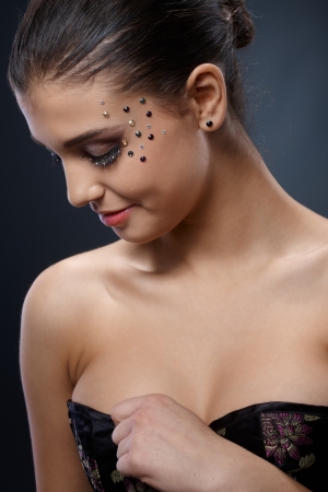 Smiling beauty in rhinestones makeup checking dress cleavage, looking down, sexy portrait.の写真素材